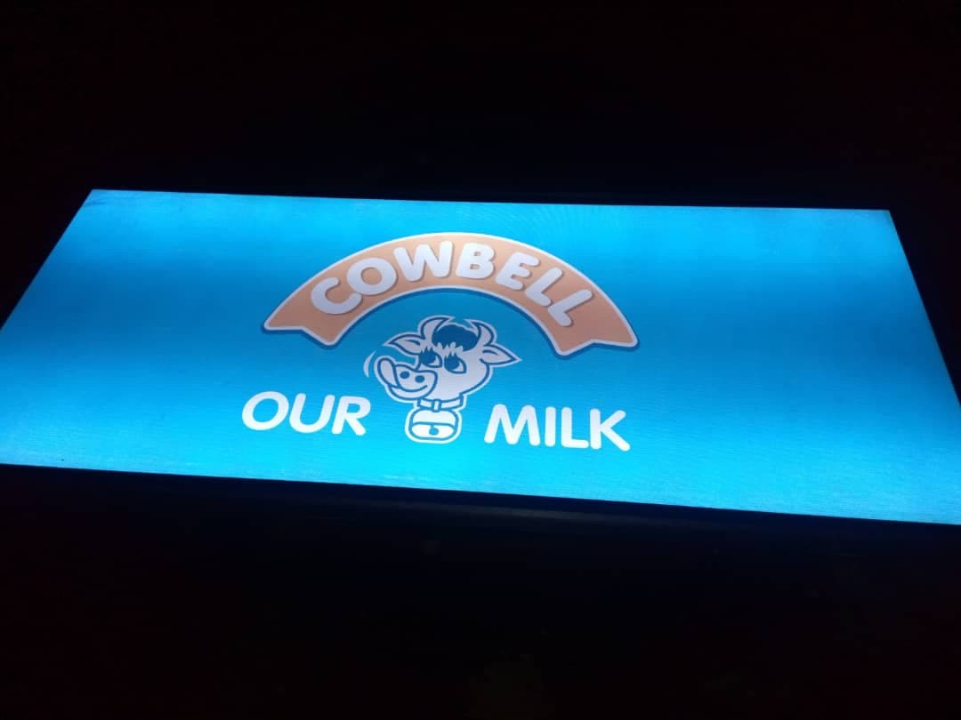 Cowbell — "Our Milk" illuminated light box, shown at night.